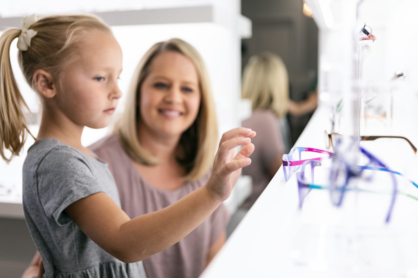 A young girl picking out her new glasses with her mom at Perfect Focus Eyecare
